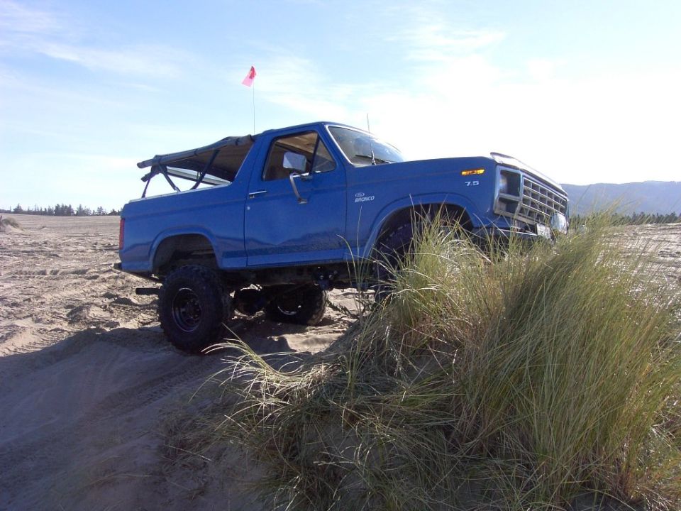 Blue lifted Ford Bronco with big tires and flag on sand dunes