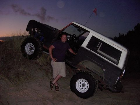 1980 Ford Bronco - A man poses next to a lifted 1980 Ford Bronco on a sand dune as the sun sets.