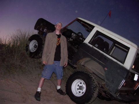 1980 Ford Bronco - Man poses with a 1980 Ford Bronco tilted on a sandy dune at dusk.