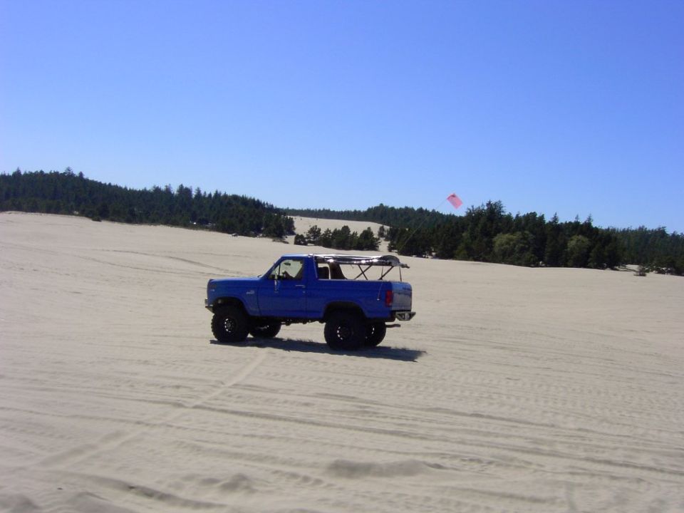 Blue lifted Ford Bronco with topless roll bar parked on sand dunes