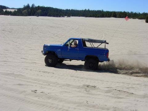 1980 Ford Bronco - Blue 1980 Ford Bronco kicking up sand while driving on a dune.