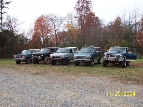 1978 Ford Bronco - A collection of Ford Broncos and trucks are lined up outdoors on a cloudy day.