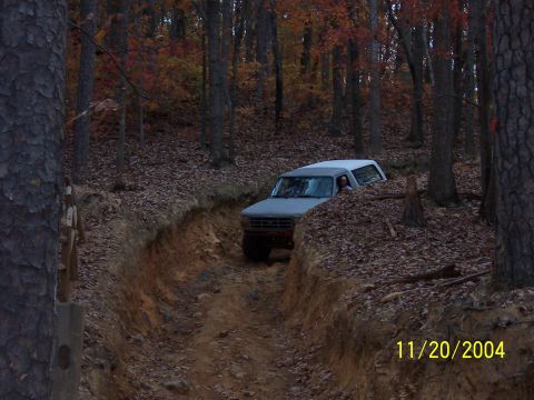 1978 Ford Bronco - A gray Ford Bronco navigates a narrow dirt path in a wooded area during autumn.