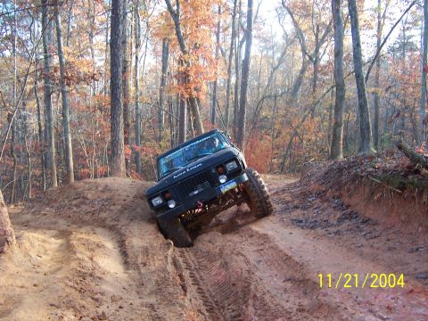 1978 Ford Bronco - An off-road vehicle navigates a muddy trail through a forest during autumn.