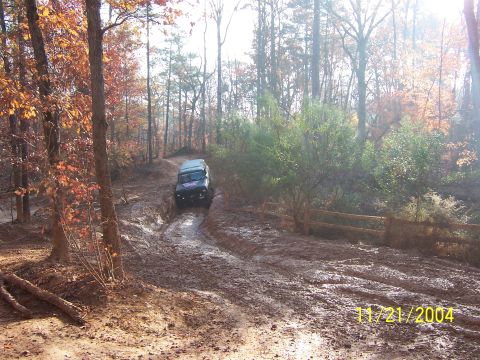 1978 Ford Bronco - A 1978 Ford Bronco tackles a challenging muddy path in a wooded area during autumn.