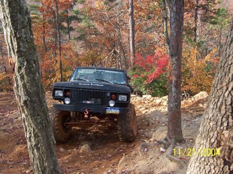 1978 Ford Bronco - A black 1978 Ford Bronco navigates a challenging off-road trail surrounded by autumn trees.