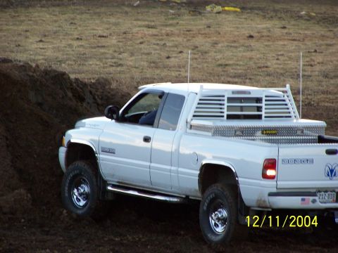 1985 Ford Bronco - A white Dodge pickup truck is shown driving on a dirt mound, equipped with a headache rack and a toolbox.