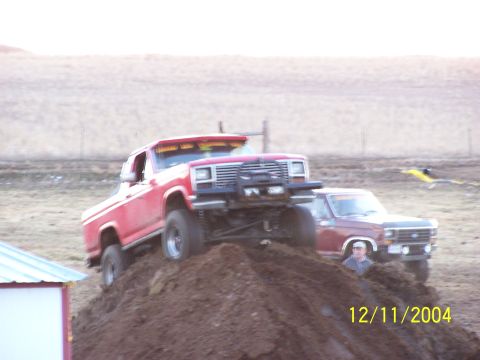 1985 Ford Bronco - A red Ford Bronco is shown climbing a dirt mound with another vehicle behind it.