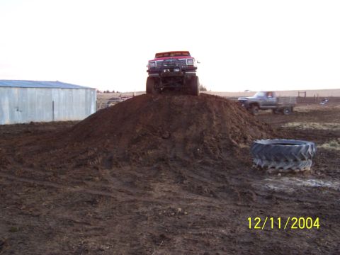 1985 Ford Bronco - Modified 1985 Ford Bronco sits atop a large dirt mound with another truck visible in the distance.