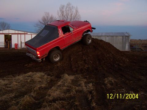 1985 Ford Bronco - A red pickup truck with a black tonneau cover navigates a steep dirt incline.