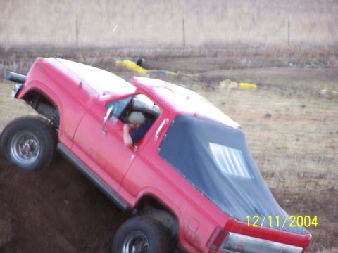 1985 Ford Bronco - A red 1985 Ford Bronco navigates an off-road incline with its driver visible.
