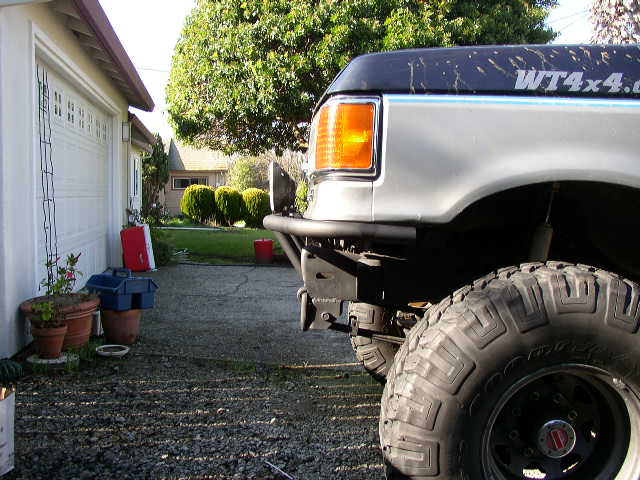 Lifted silver and blue Ford truck rear on gravel driveway with big off-road tires