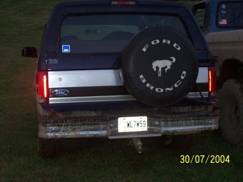 1979 Ford F-150 - Rear view of a dark blue Ford Bronco with a spare tire mounted on the back, parked next to another vehicle.