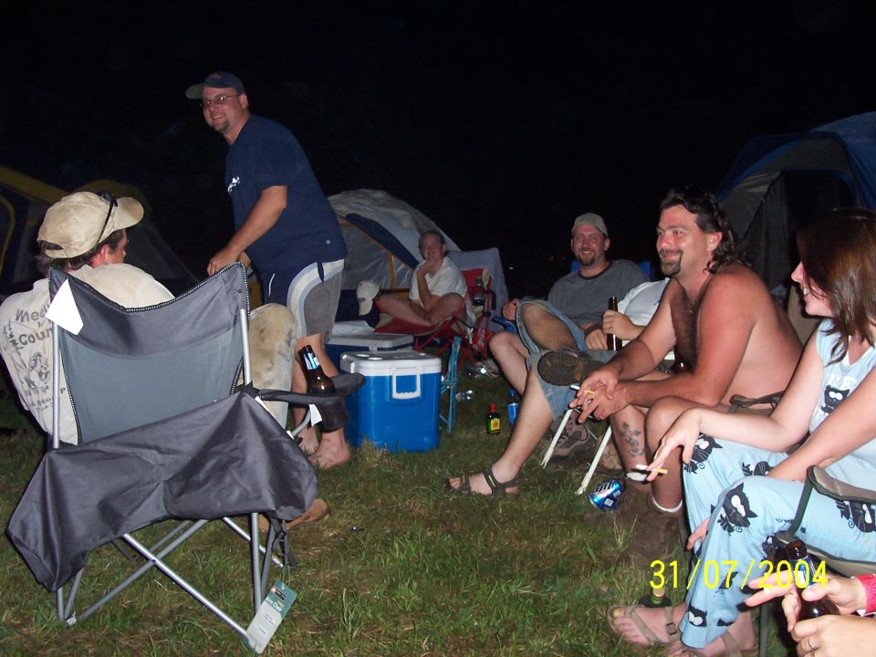 Group of people sitting in camping chairs at night with tents in the background