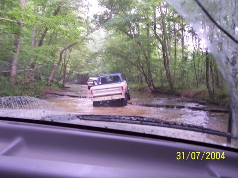 1979 Ford F-150 - Several trucks navigate a water crossing on a wooded trail.