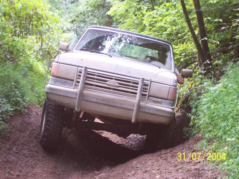 1979 Ford F-150 - A tan Ford truck navigates a steep, muddy incline surrounded by dense foliage.