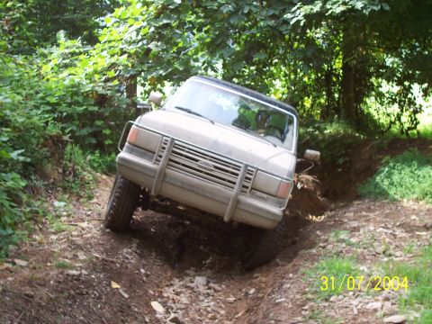 1979 Ford F-150 - A Ford Bronco II navigates a challenging off-road trail with dense foliage surrounding it.