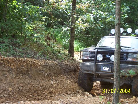 1979 Ford F-150 - A black Ford truck navigates a wooded trail with large tires and auxiliary lights.