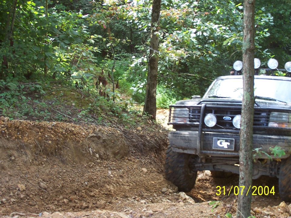 Black Ford truck with off-road tires and a brush guard, driving on a dirt path