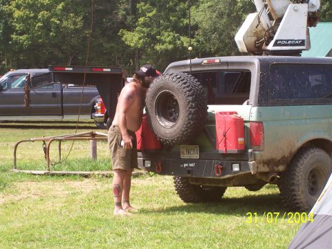 1979 Ford F-150 - Man inspects spare tire on modified SUV with jerry cans. Another truck and trailer in background.