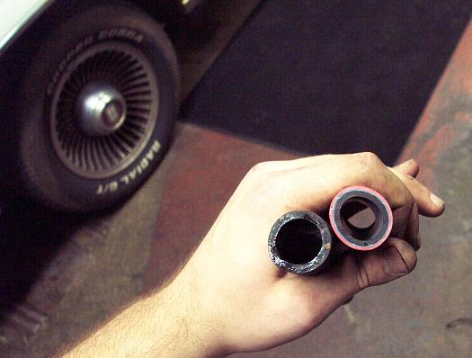 Hand holding two hoses, with a car wheel and fender in the background