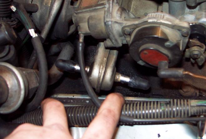 Close-up of engine bay with hoses and carburetor components. Fingers are visible in the foreground
