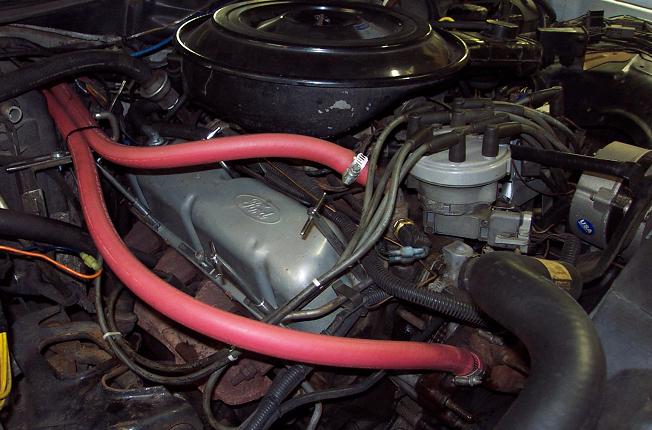 Engine bay with red heater hoses and Ford valve cover. Registry claims 1985 Ford Crown Victoria LTD
