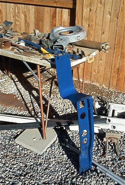 1986 Ford Bronco - Various automotive parts are laid out on a table and the ground, including a blue painted bracket.
