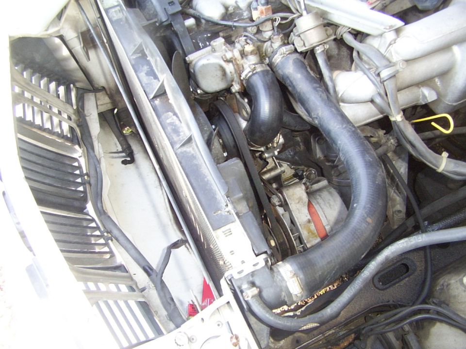 Engine bay with radiator, hoses, and belts visible. Some dirt and debris present