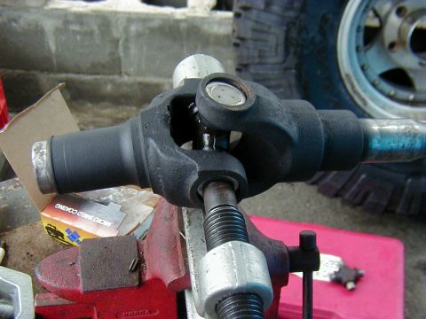 1991 Ford Bronco - Close-up of a driveshaft U-joint being pressed out with a C-clamp style universal-joint press over a red bench vise, one cap already driven…