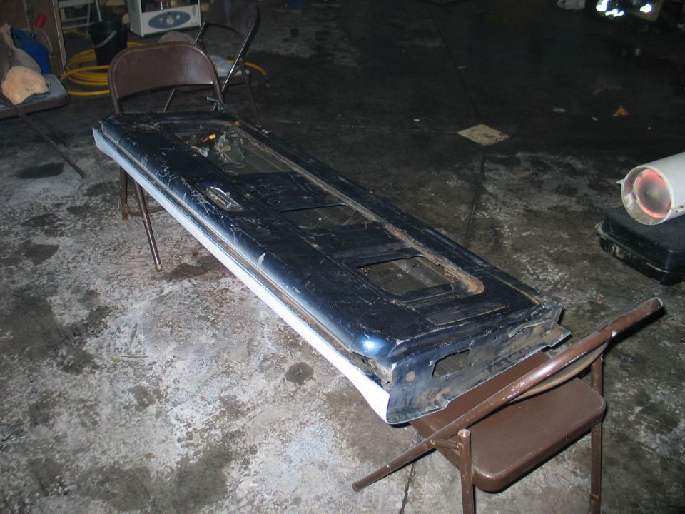 Removed blue and white truck tailgate resting inside-up on folding chairs in a garage, rusty inner skin
