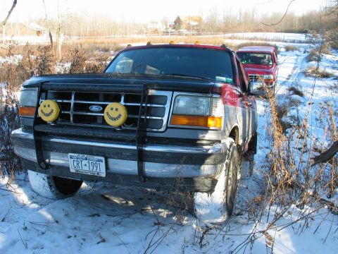 1995 Ford Bronco - A red and gray Ford F-Series truck is seen in the snow, with another red truck behind it on a dirt road.