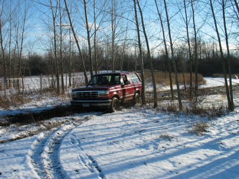 1995 Ford Bronco - A red 1995 Ford Bronco navigates a snowy and muddy path surrounded by bare trees.