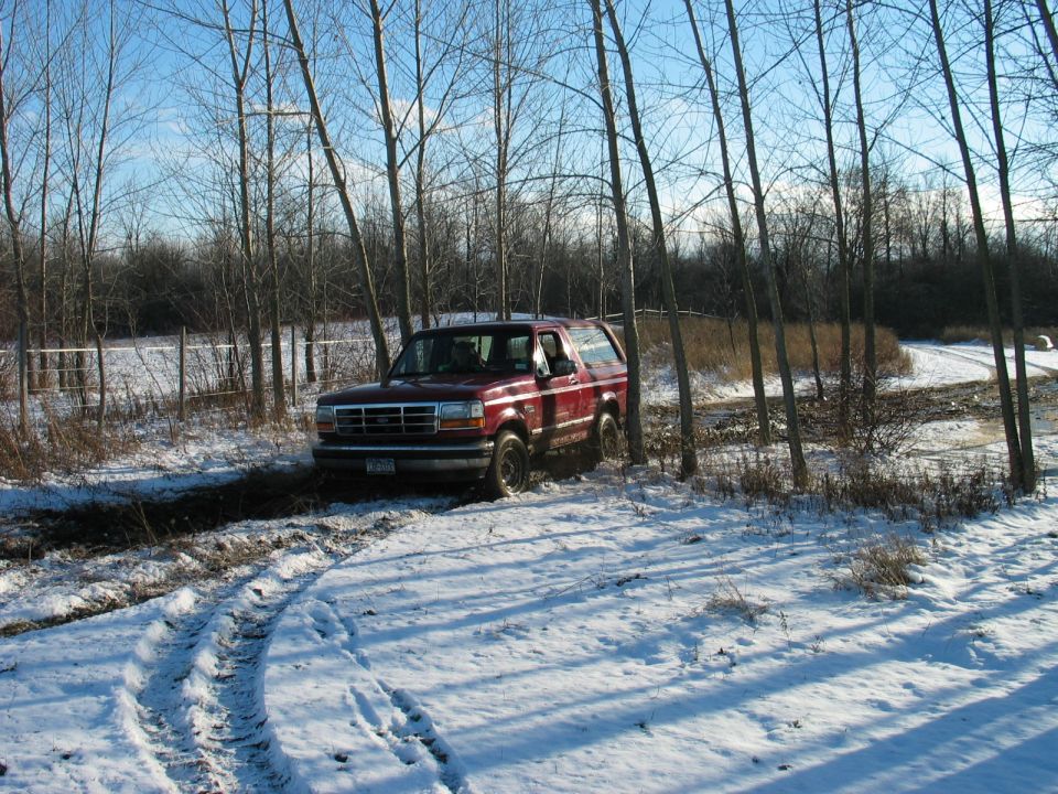 Red 1995 Ford Bronco driving through snow and mud