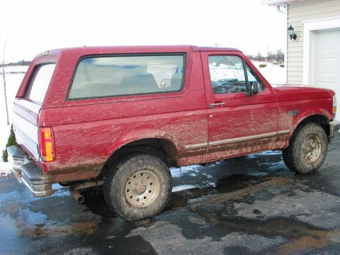 1995 Ford Bronco - This red 1995 Ford Bronco is parked outside a garage, showing signs of recent off-road use.