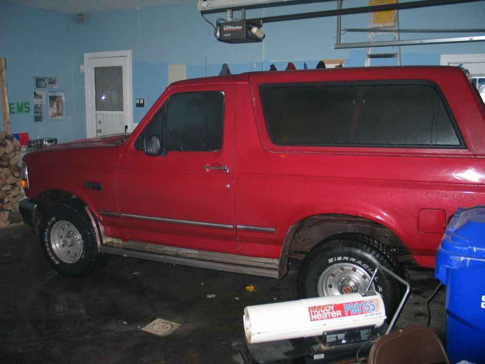 Red Ford Bronco parked inside a garage, side view. Visible text on heater