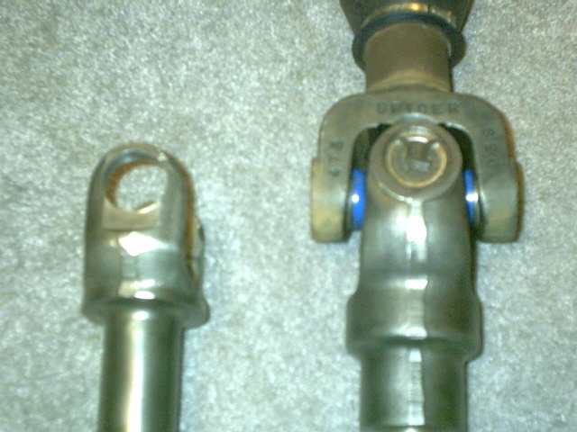 Two driveshaft yokes compared on carpet; the larger Spicer shaft has a U-joint with blue seals