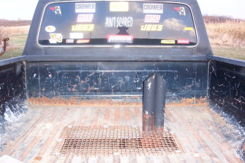 Black pickup bed with exhaust stack through mesh grate; rear window covered in racing decals