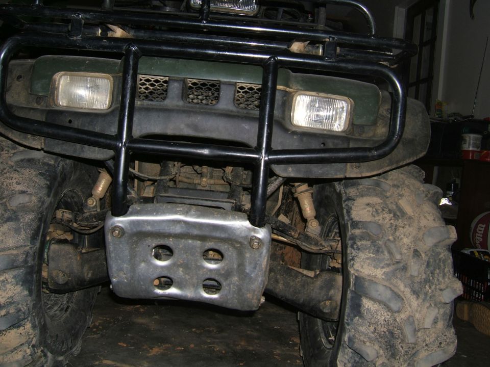 Front view of a green ATV with a black brush guard and skid plate