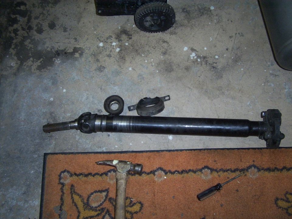 Driveshaft with U-joints, center support bearing, and rubber isolator, along with a hammer and screwdriver