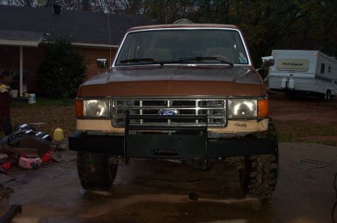 1987 Ford Bronco - The front of a 1987 Ford Bronco is shown with a new bumper and grille, parked in a driveway with a trailer behind it.