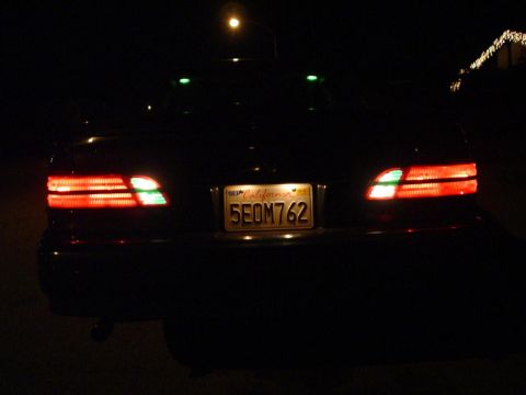 1993 Ford Taurus - The rear of a dark-colored sedan is illuminated by its red taillights and a license plate at night.