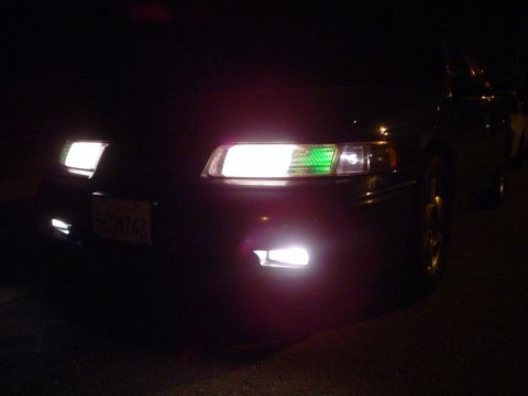 1993 Ford Taurus - Front view of a dark sedan at night, with illuminated headlights and a green turn signal visible.