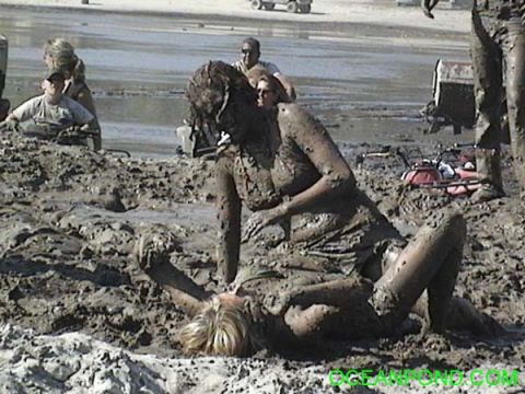 1993 Ford Bronco - Two individuals are covered in mud, with others and vehicles in the background of a muddy outdoor scene.
