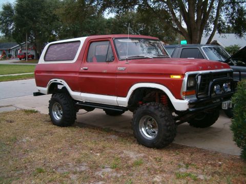 1979 Ford Bronco - A red and white lifted Ford Bronco is parked on a residential driveway next to another vehicle.