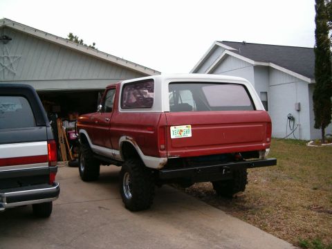 1979 Ford Bronco - This red and white 1979 Ford Bronco features a lifted suspension and off-road tires, seen from the rear.