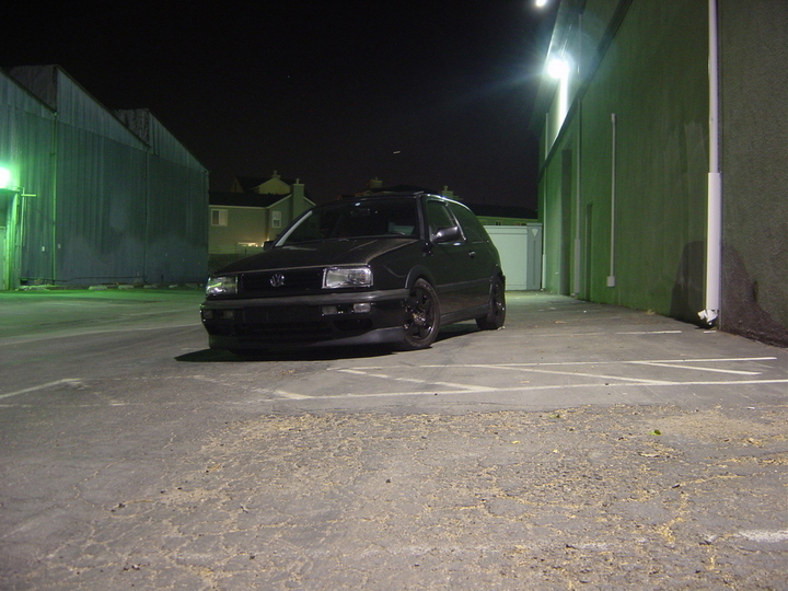 Black Volkswagen Golf Mk3 parked in a lot at night. The grille and headlight design are visible