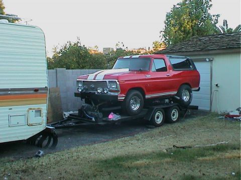 1979 Ford Bronco - A red Ford Bronco is loaded onto a trailer, parked next to a camper and a garage.