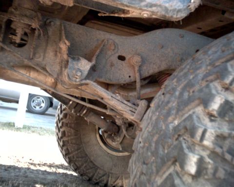 1990 Ford Bronco - The underside of a vehicle is shown, focusing on the rear suspension components and a tire, with another vehicle in the distance.