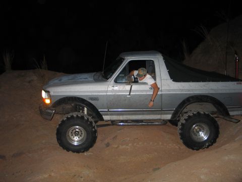 1992 Ford Bronco - Night side shot of a lifted silver 1992-1996 Ford Bronco with the fiberglass rear top replaced by a black soft bikini/cargo cover, riding o…